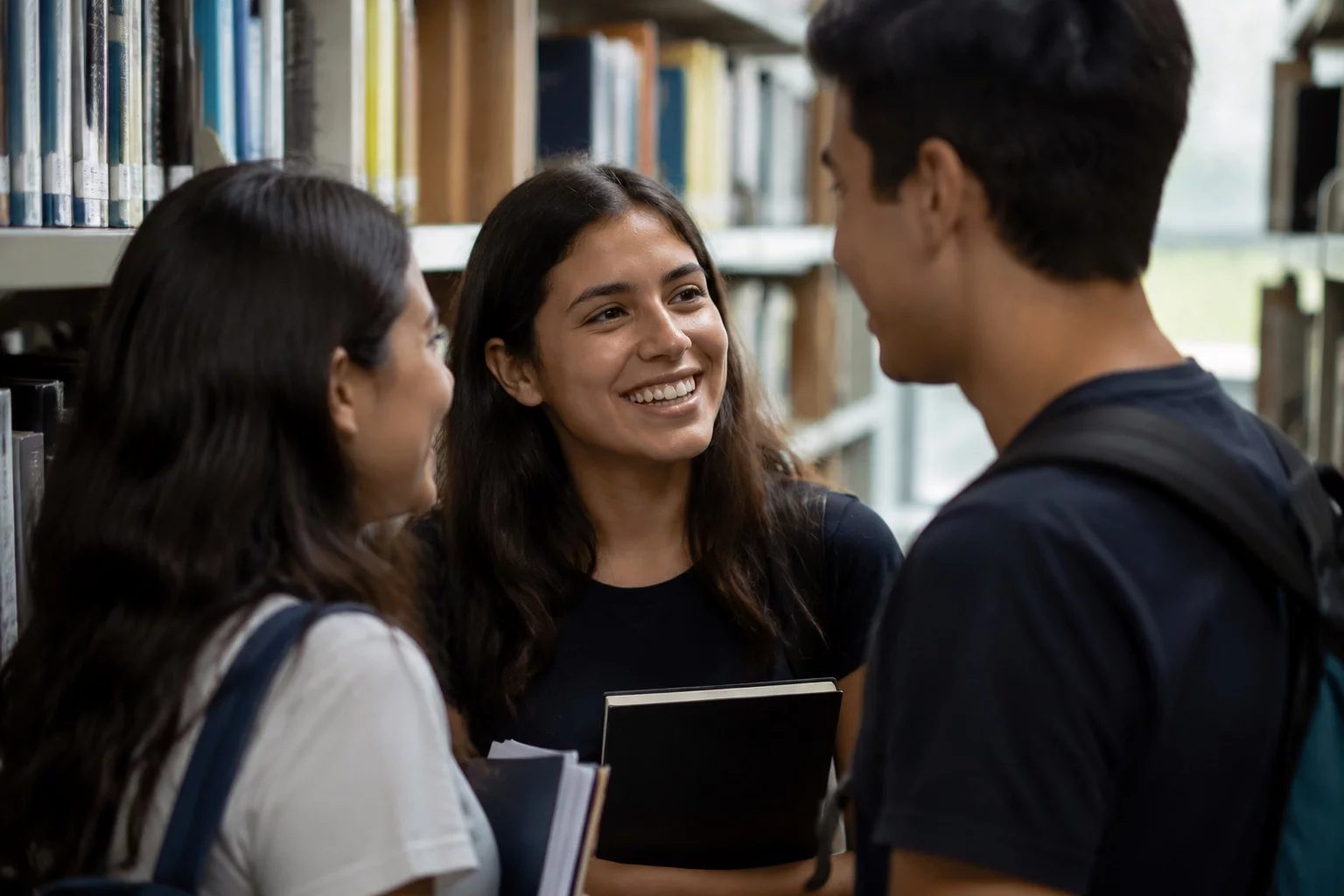 Estudantes conversando em pé entre as estantes de uma biblioteca